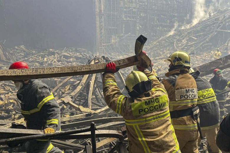 Una fotografía tomada de un vídeo distribuido por el Ministerio de Emergencias de Rusia muestra a los bomberos examinando los escombros en la sala quemada de la sala de conciertos Crocus City Hall.