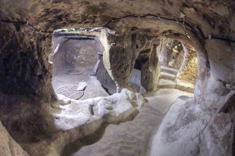 cambiando de manos de los frigios a los persas a los cristianos de la era bizantina. Finalmente fue abandonada en la década de 1920 por los griegos de Capadocia cuando enfrentaron la derrota durante la guerra greco-turca y huyeron abruptamente en masa a Grecia. Una habitación dentro de la ciudad subterráneaFUENTE DE LA IMAGEN,GETTY IMAGES No solo sus habitaciones con forma de cueva se extienden por cientos de kilómetros, sino que se cree que las más de 200 pequeñas ciudades subterráneas separadas que también se han descubierto en la región pueden estar conectadas a estos túneles, creando una red subterránea masiva. Según mi guía, Suleman, Derinkuyu solo fue «redescubierto» en 1963 por un lugareño anónimo al que constantemente se le perdían sus pollos. Mientras renovaba su casa, las aves de corral desaparecían en una pequeña grieta creada durante la remodelación y nunca más se las volvía a ver. Tras una investigación más detallada y algunas excavaciones, el turco descubrió un pasadizo oscuro. Fue la primera de más de 600 entradas encontradas dentro de casas particulares que conducen a la ciudad subterránea de Derinkuyu. Civilización escondida La excavación comenzó de inmediato, revelando una red enredada de viviendas subterráneas, almacenamiento de alimentos secos, establos de ganado, escuelas, bodegas e incluso una capilla. Era toda una civilización escondida a salvo bajo tierra. La ciudad cueva pronto fue visitada por miles de los turistas menos claustrofóbicos de Turquía y, en 1985, la región se agregó a la lista del Patrimonio Mundial de la Unesco. Vista de túneles bajo tierraFUENTE DE LA IMAGEN,GETTY IMAGES Pie de foto,Derinkuyu se compone de 18 niveles de túneles. La fecha exacta de construcción de la ciudad sigue siendo discutida, pero «Anabasis», escrita por Jenofonte de Atenas alrededor del 370 a.C., es la obra escrita más antigua que parece hacer referencia a Derinkuyu. En el libro, menciona a la gente de Anatolia, en o cerca de la región de Capadocia, que vive bajo tierra en casas excavadas en lugar de en las más populares cuevas cavadas en los acantilados también bastante conocidas en la zona.