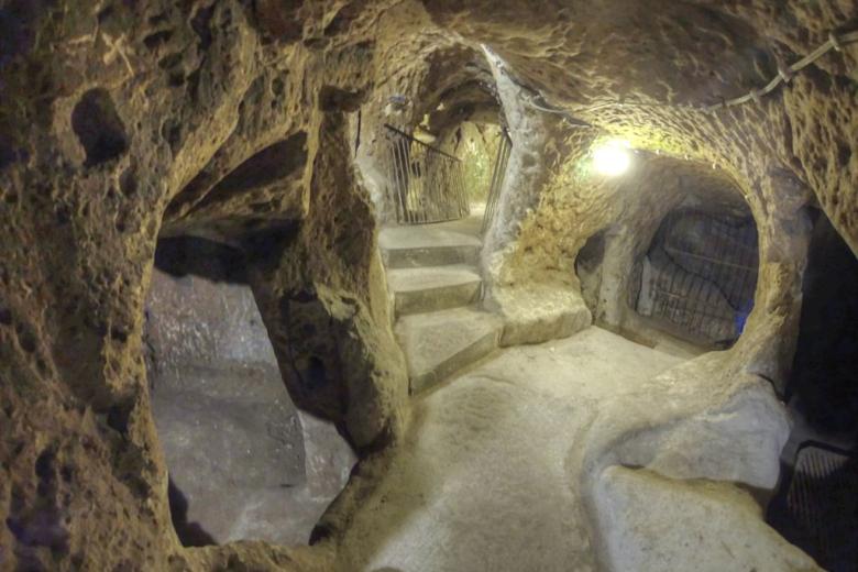 No solo sus habitaciones con forma de cueva se extienden por cientos de kilómetros, sino que se cree que las más de 200 pequeñas ciudades subterráneas separadas que también se han descubierto en la región pueden estar conectadas a estos túneles, creando una red subterránea masiva. Según mi guía, Suleman, Derinkuyu solo fue «redescubierto» en 1963 por un lugareño anónimo al que constantemente se le perdían sus pollos. Mientras renovaba su casa, las aves de corral desaparecían en una pequeña grieta creada durante la remodelación y nunca más se las volvía a ver. Tras una investigación más detallada y algunas excavaciones, el turco descubrió un pasadizo oscuro. Fue la primera de más de 600 entradas encontradas dentro de casas particulares que conducen a la ciudad subterránea de Derinkuyu. Civilización escondida La excavación comenzó de inmediato, revelando una red enredada de viviendas subterráneas, almacenamiento de alimentos secos, establos de ganado, escuelas, bodegas e incluso una capilla. Era toda una civilización escondida a salvo bajo tierra. La ciudad cueva pronto fue visitada por miles de los turistas menos claustrofóbicos de Turquía y, en 1985, la región se agregó a la lista del Patrimonio Mundial de la Unesco. Vista de túneles bajo tierraFUENTE DE LA IMAGEN,GETTY IMAGES Pie de foto,Derinkuyu se compone de 18 niveles de túneles. La fecha exacta de construcción de la ciudad sigue siendo discutida, pero «Anabasis», escrita por Jenofonte de Atenas alrededor del 370 a.C., es la obra escrita más antigua que parece hacer referencia a Derinkuyu. En el libro, menciona a la gente de Anatolia, en o cerca de la región de Capadocia, que vive bajo tierra en casas excavadas en lugar de en las más populares cuevas cavadas en los acantilados también bastante conocidas en la zona.