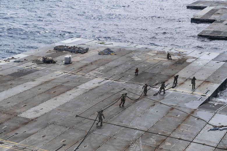 U.S. Army Soldiers assigned to the 7th Transportation Brigade (Expeditionary) handle line to secure the Roll-On, Roll-Off Distribution Facility (RRDF), or floating pier, to the side of the MV Roy P. Benavidez, in support of Joint Logistics Over-The-Shore (JLOTS) operations off the coast of Gaza, May 1, 2024. The temporary pier will assist the United States Agency for International Development in the delivery of humanitarian aid to the people of Gaza, which will increase the quantity and flow of humanitarian aid, including food, water, medicine, and temporary shelters. (U.S. Navy photo)