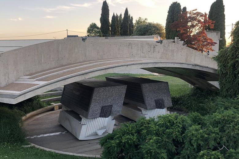 De hecho, el escenógrafo Patrice Vermette, ganador de un Oscar, decidió ambientar algunas escenas en el edificio situado en San Vito di Altivole, en la llanura de Treviso, entre Castelfranco y Asolo, declarado patrimonio de la FAI desde 2022. El Memorial Brion, como también se le conoce, es la tumba de Giuseppe Brion, el fundador de Brionvega, y su esposa Onorina. Construido entre 1969 y 1978, es también la última obra del gran arquitecto veneciano, que fue enterrado aquí. Una obra maestra que combina hormigón armado y una dimensión arcaica y futurista, inmersa en un inconfundible aura oriental y, en particular, japonesa. De hecho, la Tumba de Brion tiene un sabor "extraterrestre". Se trata de un conjunto de edificios dispuestos en un jardín en forma de L, salpicado de canales, senderos, estanques y podios de piedra, al que se accede cruzando propileos abiertos por dos círculos entrelazados. El recorrido es laberíntico, lleno de cortes y sugerencias acentuadas por decoraciones geométricas, planos facetados, elementos alusivos. El sabor arcano se ve acentuado por la presencia constante de agua. Los sarcófagos del matrimonio Brion, esculturas abstractas inclinadas una hacia la otra, están dispuestos bajo un gran arcosolio. La capilla, elegida como escenario para "Dune - Part 2", está creada en un cuadrado girado 45° dentro de un edificio más grande. Aquí es donde la princesa Irulan, la hija del emperador, se sienta en un escritorio en varias escenas de la película.