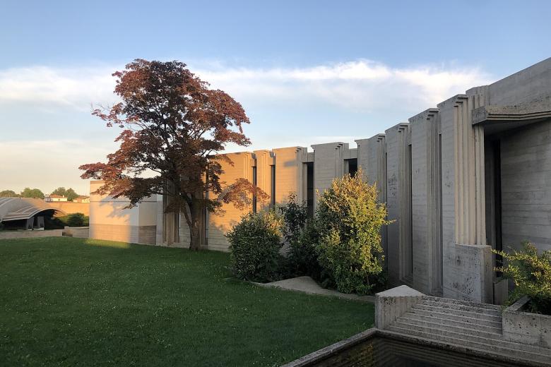 El Memorial Brion, como también se le conoce, es la tumba de Giuseppe Brion, el fundador de Brionvega, y su esposa Onorina. Construido entre 1969 y 1978, es también la última obra del gran arquitecto veneciano, que fue enterrado aquí. Una obra maestra que combina hormigón armado y una dimensión arcaica y futurista, inmersa en un inconfundible aura oriental y, en particular, japonesa. De hecho, la Tumba de Brion tiene un sabor "extraterrestre". Se trata de un conjunto de edificios dispuestos en un jardín en forma de L, salpicado de canales, senderos, estanques y podios de piedra, al que se accede cruzando propileos abiertos por dos círculos entrelazados. El recorrido es laberíntico, lleno de cortes y sugerencias acentuadas por decoraciones geométricas, planos facetados, elementos alusivos. El sabor arcano se ve acentuado por la presencia constante de agua. Los sarcófagos del matrimonio Brion, esculturas abstractas inclinadas una hacia la otra, están dispuestos bajo un gran arcosolio. La capilla, elegida como escenario para "Dune - Part 2", está creada en un cuadrado girado 45° dentro de un edificio más grande. Aquí es donde la princesa Irulan, la hija del emperador, se sienta en un escritorio en varias escenas de la película.