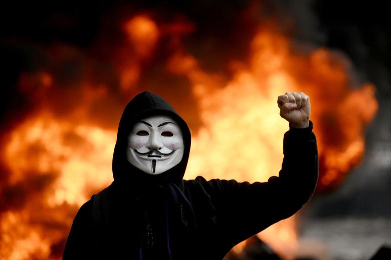 Un manifestante con una máscara camina frente a un automóvil de la estación de radio Cadena 3 incendiado en una calle cercana al Congreso argentina