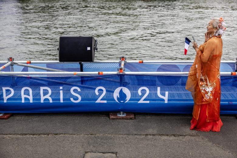 Smoke in the colours of the France flag are set off as people gather on a bridge over the Seine River in Paris, France, at the start of the opening ceremony for the 2024 Summer Olympics, Friday, July 26, 2024. (Photo by Bernat Armangue / POOL / AFP)