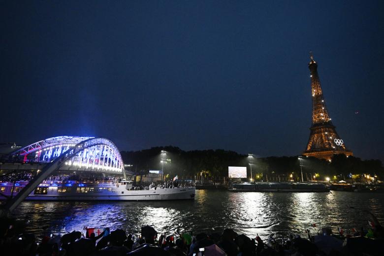 Los atletas de la delegación francesa navegan en un bote por el puente Passerelle Debilly a lo largo del río Sena