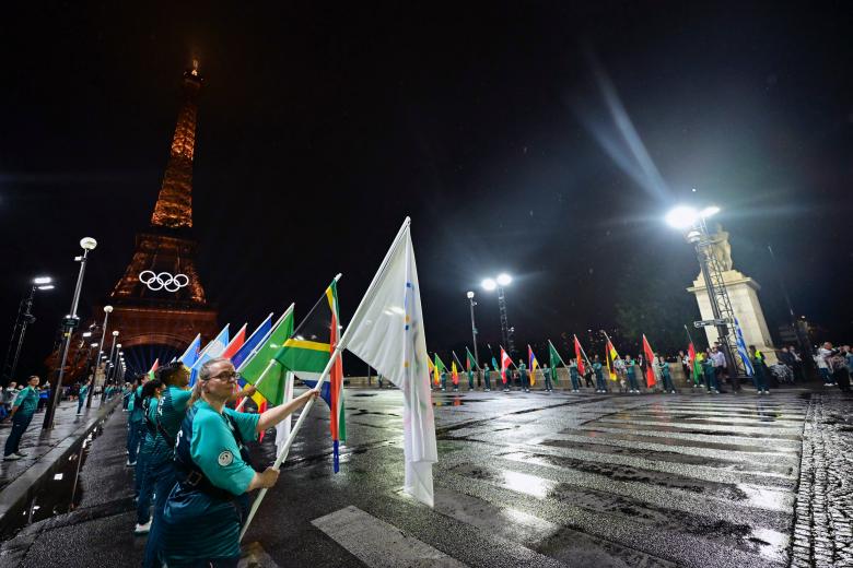 Voluntarios portan banderas de los equipos olímpicos en el puente de Iena durante la ceremonia de apertura de los Juegos Olímpicos de París 2024