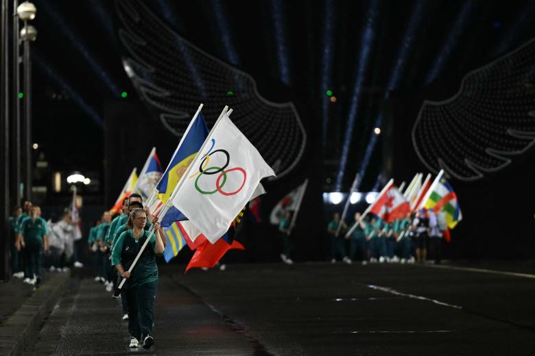 Voluntarios portan banderas de los equipos olímpicos en el puente de Iena durante la ceremonia de apertura de los Juegos Olímpicos de París 2024