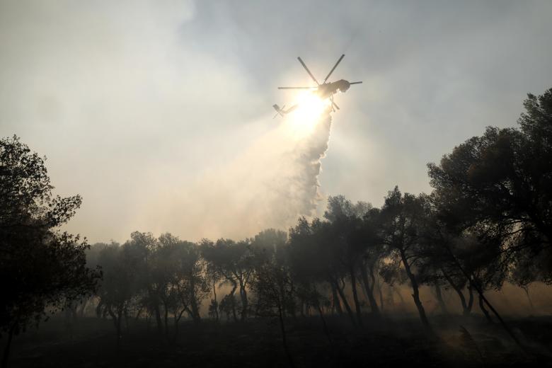 Un helicóptero esparce agua sobre un incendio este lunes en Patima Halandri, a las afueras de Atenas