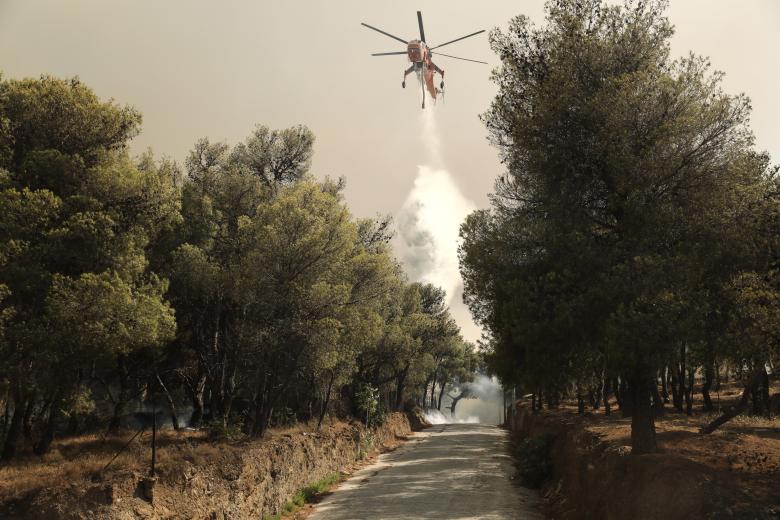 Un helicóptero lanza agua para intentar controlar las llamas a las afueras de Atenas