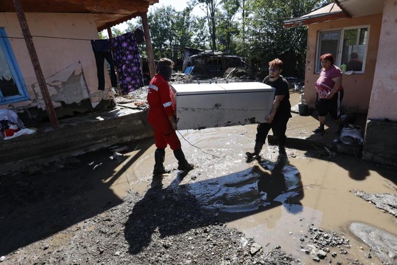 Mihaela (derecha), de 51 años, observa cómo dos voluntarios llevan su refrigerador después de una inundación en el pueblo de Slobozia Conachi, cerca de la ciudad de Galati, Rumania.