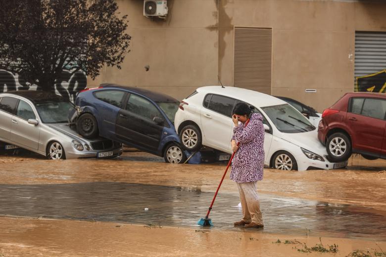 Una mujer realiza labores de limpieza junto a vehículos destrozados tras el paso de la DANA por el barrio de La Torre de Valencia