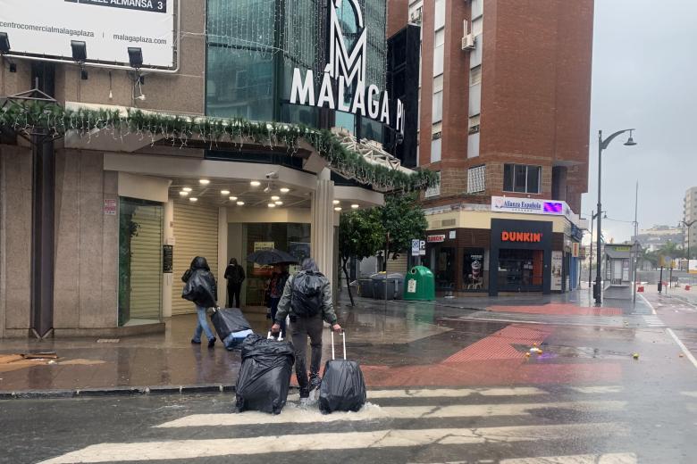 Unos turistas con las maletas tapadas con bolsas caminan por una calle de Málaga, este miércoles en el que las fuertes trombas de agua y granizo que se han registrado han causado inundaciones y la acumulación de grandes balsas en algunas de las principales avenidas de todos los distritos de la ciudad. EFE/Montserrat Martínez