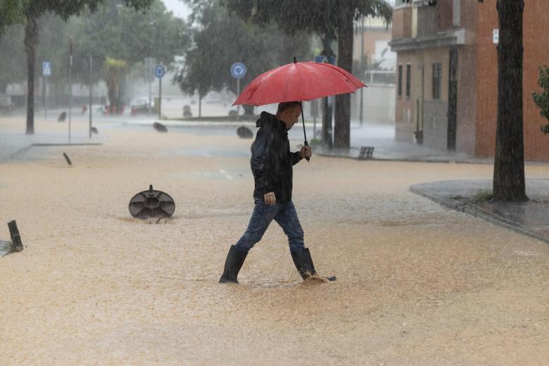 Un hombre caminando por una calle en la barriada de Campanillas en Málaga, en la que el paso de la dana ha obligado a nuevos desalojos preventivos en el río Campanillas ante su posible desbordamiento.  la mayor parte de la provincia malagueña se encuentra en aviso rojo por fuertes lluvias.