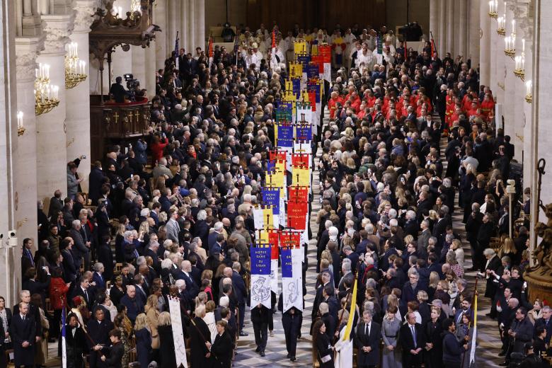 Los invitados se paran mientras desfilan los estandartes de la Iglesia durante una ceremonia para marcar la reapertura de la histórica Catedral de Notre Dame