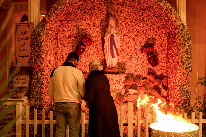 Una pareja musulmana junto a la hoguera ante el santuario de la Virgen María durante el servicio de Nochebuena en la catedral católica siríaca del Sagrado Corazón en la ciudad meridional iraquí de Basora el 24 de diciembre de 2024