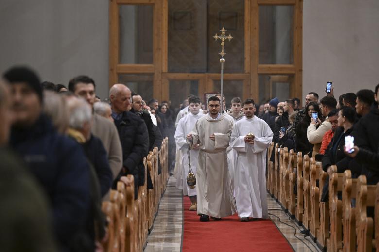 Una pareja musulmana junto a la hoguera ante el santuario de la Virgen María durante el servicio de Nochebuena en la catedral católica siríaca del Sagrado Corazón en la ciudad meridional iraquí de Basora el 24 de diciembre de 2024