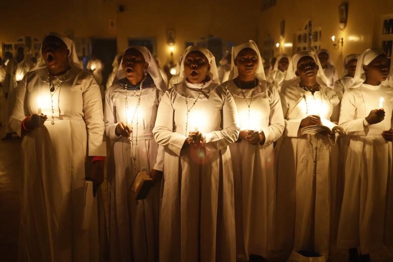 Una pareja musulmana junto a la hoguera ante el santuario de la Virgen María durante el servicio de Nochebuena en la catedral católica siríaca del Sagrado Corazón en la ciudad meridional iraquí de Basora el 24 de diciembre de 2024