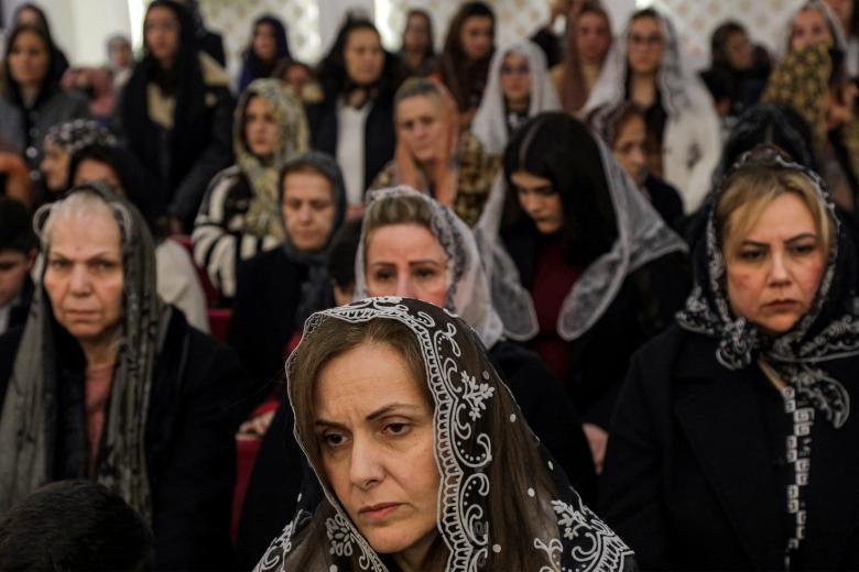 Una pareja musulmana junto a la hoguera ante el santuario de la Virgen María durante el servicio de Nochebuena en la catedral católica siríaca del Sagrado Corazón en la ciudad meridional iraquí de Basora el 24 de diciembre de 2024