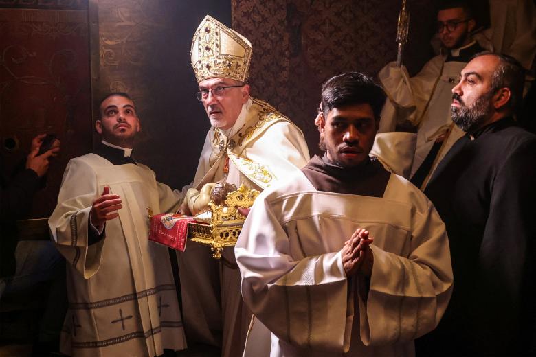 Una pareja musulmana junto a la hoguera ante el santuario de la Virgen María durante el servicio de Nochebuena en la catedral católica siríaca del Sagrado Corazón en la ciudad meridional iraquí de Basora el 24 de diciembre de 2024