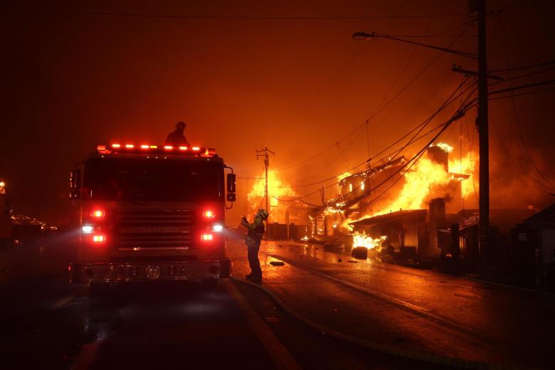 Los bomberos trabajan mientras el incendio forestal de Palisades quema varias estructuras a lo largo de la Pacific Coast Highway en Malibú