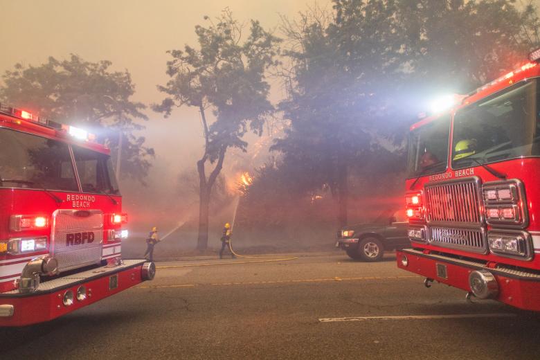 Un bombero rocía agua mientras las llamas del incendio Palisades arden en Sunset Boulevard durante una poderosa tormenta de viento el 7 de enero