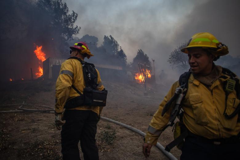 Los bomberos observan las llamas del incendio Palisades que arde frente al templo judío Chabah de Pacific Palisades