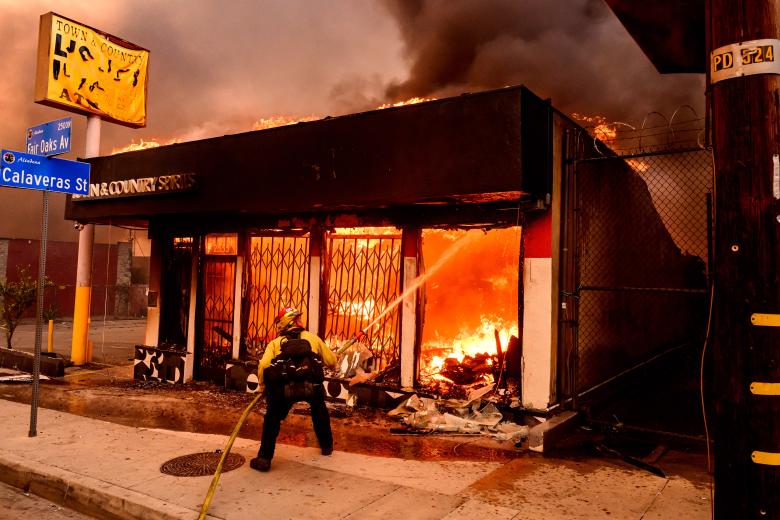 Un bombero apaga las llamas mientras una licorería arde durante el incendio de Eaton en Altadena