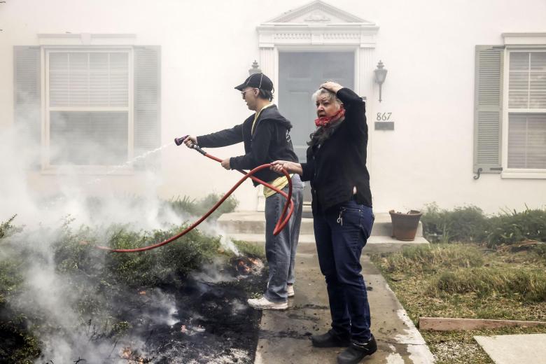 Dos personas trabajan para extinguir los puntos calientes en el patio de un vecino con una manguera de jardín