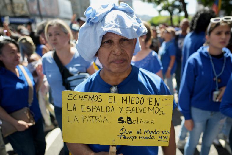 Un hombre sostiene un cartel con una cita del libertador Simón Bolívar que dice 'Pongámonos el miedo en la espalda y salvemos la patria', durante una protesta convocada por la oposición en vísperas de la toma de posesión presidencial en Caracas