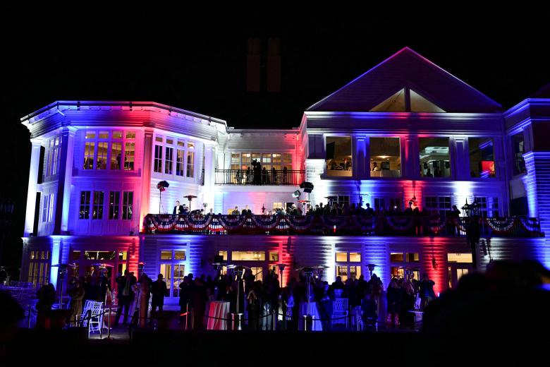 La casa club blanca se ilumina en rojo, blanco y azul mientras el presidente electo de EE.UU. Donald Trump y su esposa Melania Trump ven fuegos artificiales durante una recepción en su honor en el Trump National Golf Club Washington DC en Sterling, Virginia,