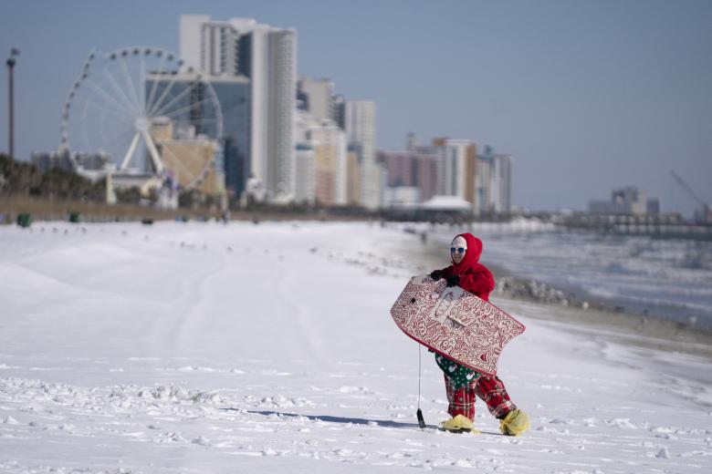 Un niña con una tabla de surf en una playa nevada de  Myrtle Beach, en Carolina del Sur