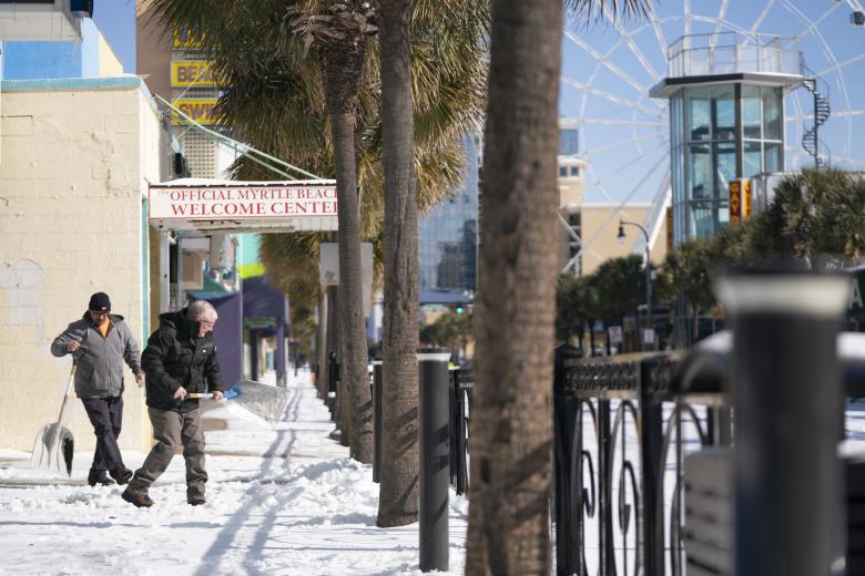 Hombres quitan la nieve de una acera a lo largo de North Ocean Boulevard el 22 de enero de 2025 en Myrtle Beach, Carolina del Sur