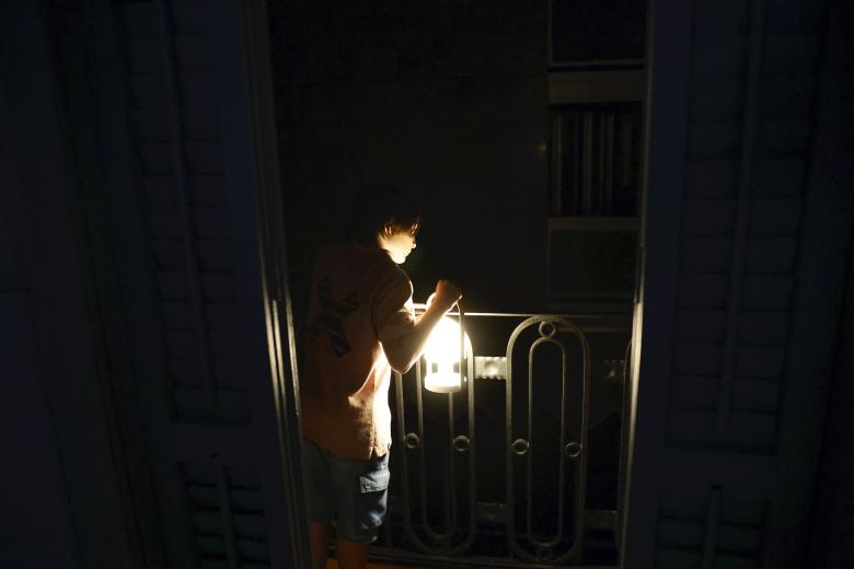 Un niño con una lampara mira desde el balcón la calle todavía a oscuras esta madrugada en el centro de Barcelona durante el corte de suministro eléctrico