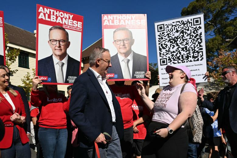 A woman holds a sausage, known casually as a "democracy sausage", as she poses beside a person dressed as a bottle of "democracy sauce" at a polling station for the general election in a primary school in the suburb of Marrickville in Sydney on May 3, 2025. Millions of Australians voted on May 3 in a bitterly contested general election, following a campaign shaped by living costs, climate anxiety and US President Donald Trump's tariffs. (Photo by DAVID GRAY / AFP)