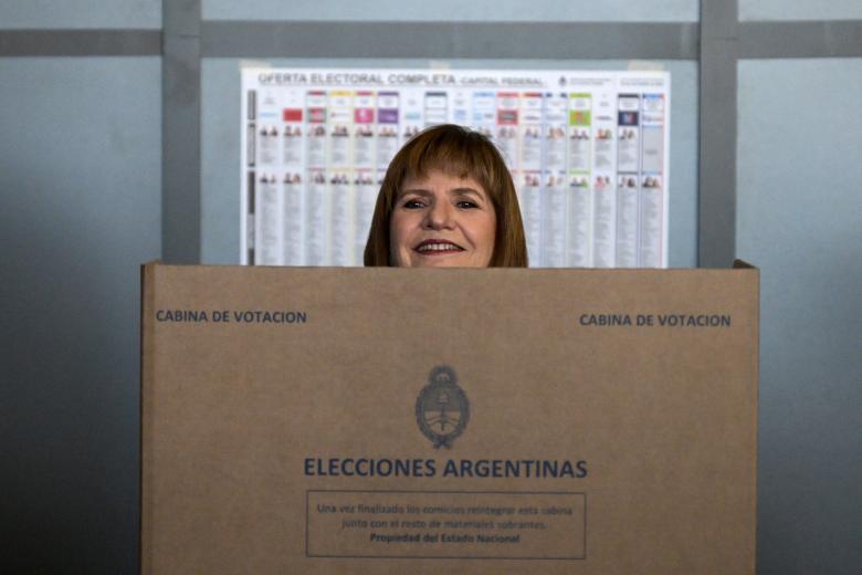 A man with a baby looks at the election options on a bulletin board at a polling station during the national midterm legislative election in Buenos Aires on October 26, 2025. Argentines head to the polls for a midterm election that will determine whether President Javier Milei enters the second half of his term bolstered or diminished as economic troubles abound despite unprecedented US aid. (Photo by JUAN MABROMATA / AFP)