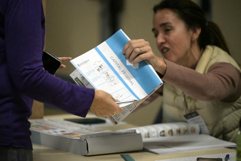 A voter receives a ballot during the national midterm legislative election, in Buenos Aires on October 26, 2025. Argentines head to the polls for a midterm election that will determine whether President Javier Milei enters the second half of his term bolstered or diminished as economic troubles abound despite unprecedented US aid. (Photo by Luis ROBAYO / AFP)