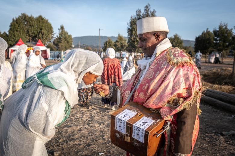 Una joven besa una cruz ofrecida por un sacerdote ortodoxo que sostiene una caja de donaciones a la entrada del lugar de celebraciones de Timkat. Una vez que los tabots se reúnen en un lugar, los sacerdotes dirigen una ceremonia de oración