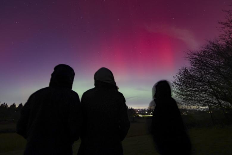 Personas observan una aurora boreal este lunes, en Essen (Alemania). El color de una aurora depende del tipo y la altitud de los gases atmosféricos golpeados por las partículas espaciales, siendo el oxígeno el que produce luz verde a menor altitud y luz roja a mayor altitud, según la NASA.