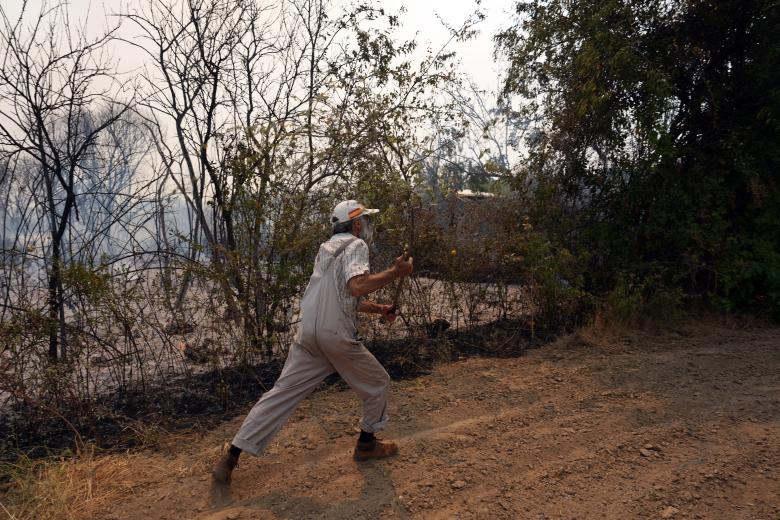 Un vecino corre para apagar unas pequeñas brasas que vuelan por los aires mientras arde un incendio forestal cerca de San Martín de Valdeiglesias, a unos 70 km al oeste de Madrid, el 26 de julio de 2026.
