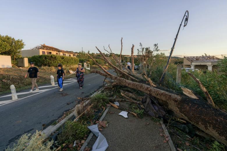 Unos peatones pasan junto a un árbol derribado y cerca de viviendas dañadas después de que un tornado azotara Pomas.