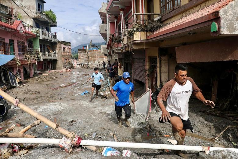 Residentes locales caminan junto a casas anegadas por el lodo tras unas inundaciones repentinas en Devighat, municipio de Bidur (distrito de Nuwakot, Nepal)