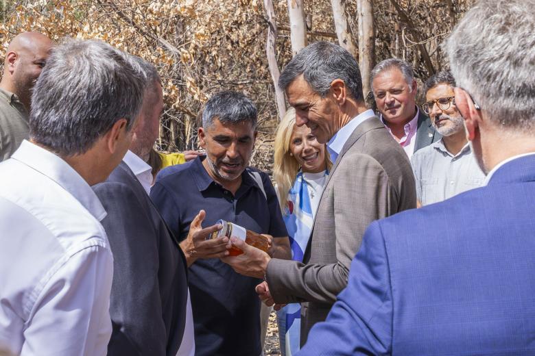 El presidente del Gobierno, Pedro Sánchez (d), recibe un bote de miel del alcalde de Berrocal, Ángel Luis Romero Romero (i), durante un encuentro con los alcaldes de los municipios afectados por el incendio de Niebla (Huelva)