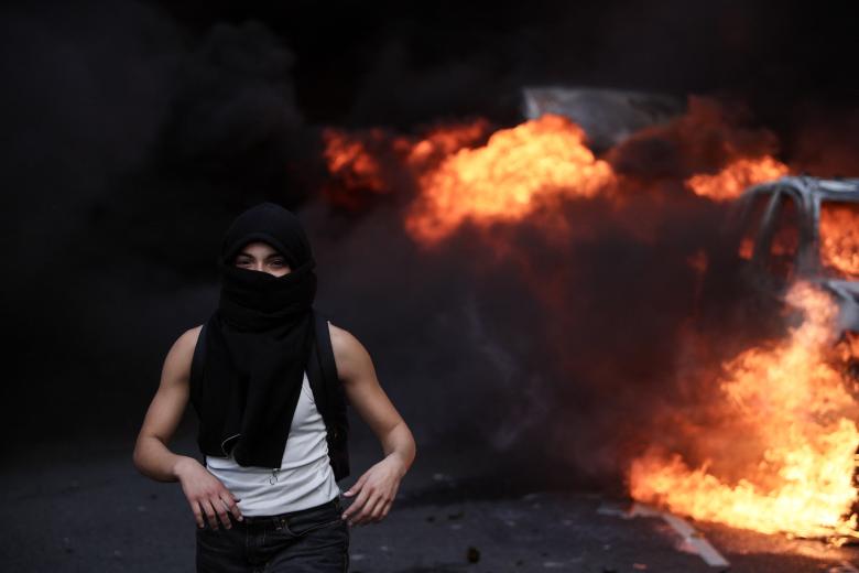 Un manifestante encapuchado en París mientras atrás un coche arde
