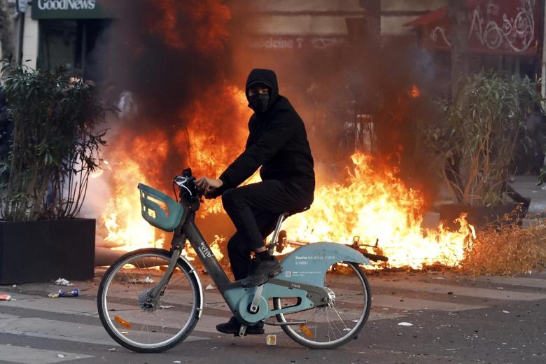 Paris (France), 17/10/2026.- A man rides a bicycle past a fire in the street during a demonstration against rising living costs and cuts to public services in Paris, France, 17 October 2026. The nationwide mobilization brought together Yellow Vest (Gilets Jaunes) activists, high school and university students, trade unions and other groups protesting rising living costs, fuel prices and deteriorating public services, while demanding improvements in education and school conditions. (Protestas, Francia) EFE/EPA/MOHAMMED BADRA