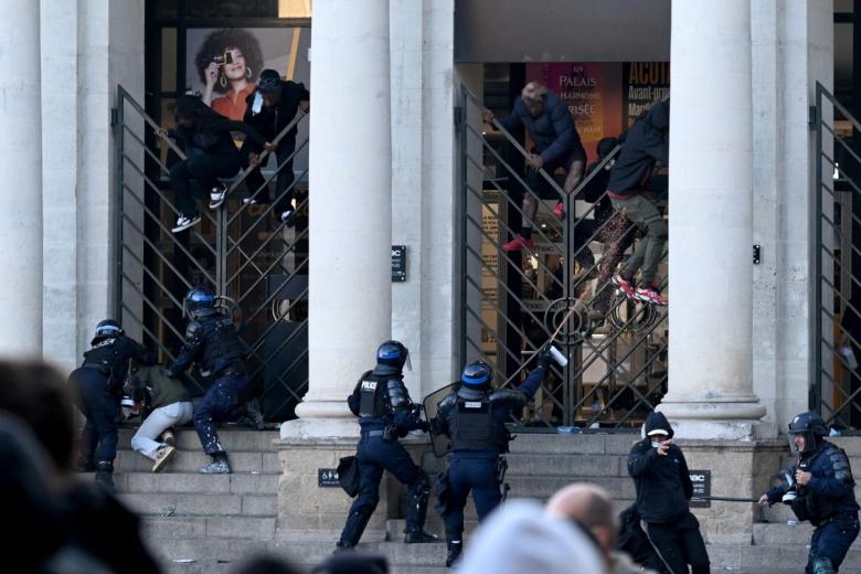 Police officers run past a fire at the Boulevard des Capucines during a demonstration to protest against the "high cost of living", in Paris on October 17, 2026 as part of a nationwide call for mobilisation bringing together various groups expressing their anger: former "Yellow Vests", secondary school and university students, climate activists and even farmers. After weeks of student protests, France faces broader, nationwide demonstrations on October 17, 2026 over the cost of living, setting up a potentially fraught six months heading into a presidential election. A police source told AFP that authorities estimated nearly 200,000 people could take part, with 40,000 in Paris. (Photo by Kiran RIDLEY / AFP)