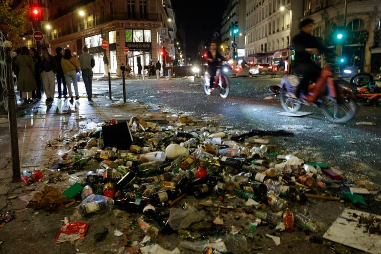 A woman walks past a broken woindow shop of Guess magazine following a demonstration against the "high cost of living", in Paris on October 17, 2026 as part of a nationwide call for mobilisation bringing together various groups expressing their anger: former "Yellow Vests", secondary school and university students, climate activists and even farmers. After weeks of student protests, France faces broader, nationwide demonstrations on October 17, 2026 over the cost of living, setting up a potentially fraught six months heading into a presidential election. A police source told AFP that authorities estimated nearly 200,000 people could take part, with 40,000 in Paris. (Photo by GEOFFROY VAN DER HASSELT / AFP)