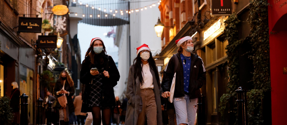 Pedestrians, some wearing face coverings to combat the spread of Covid-19, walk past shops in Covent Garden on the last Saturday for shopping before Christmas, in central London on December 18, 2021. - The British government on Friday reported 93,045 new coronavirus cases, a third consecutive record daily tally, as the Omicron variant fuels a surge in infections across the country. Britain is currently rolling out a mass booster drive in order to vaccinate as many people as possible before the end of the year. (Photo by Tolga Akmen / AFP)