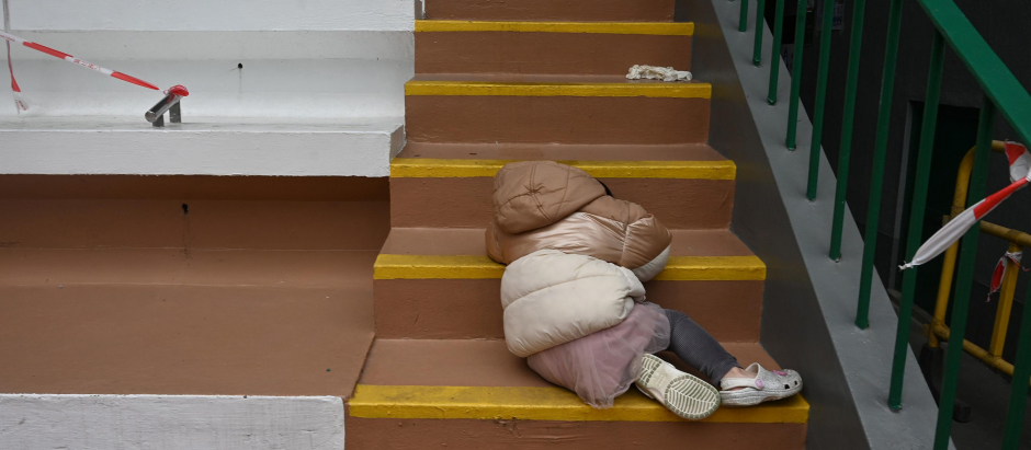 Un niño descansa sobre unas escaleras junto a su madre mientras esperan para un test de la covid en Hong Kong