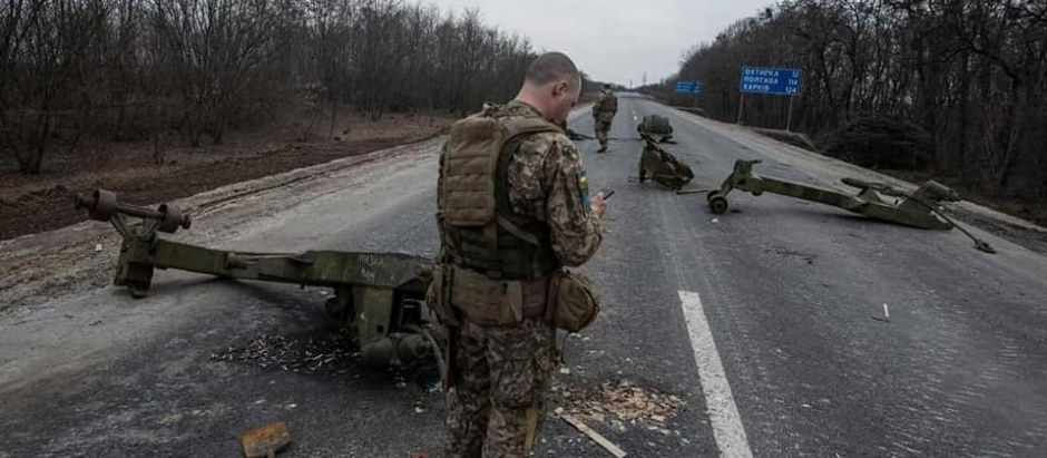 Un soldado ucraniano observa su teléfono móvil junto a un vehículo ruso destruido