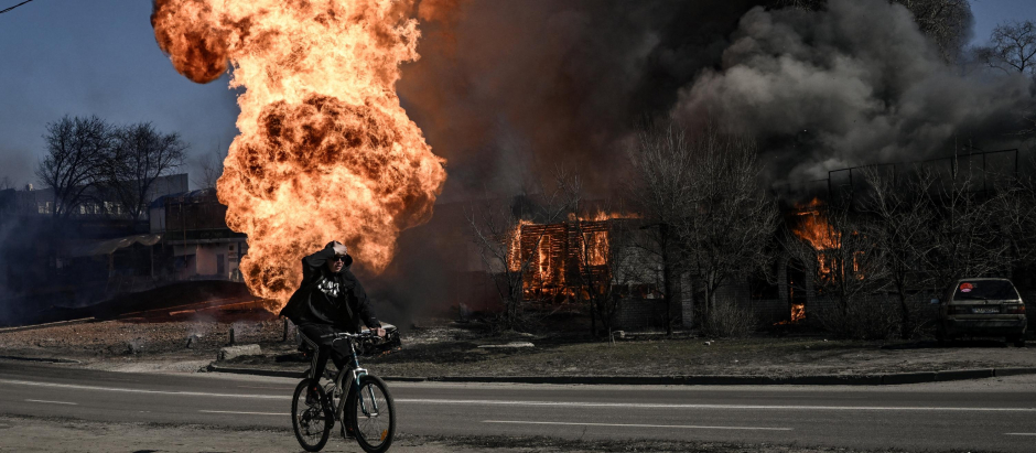 Un ciclista pedalea cerca de las llamas, vestigios de una explosión, en la ciudad ucraniana de Járkov